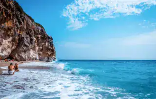 Playa en la costa albanesa con acantilados, agua azul turquesa y cielo azul, ideal para vacaciones y relax en Albania.
