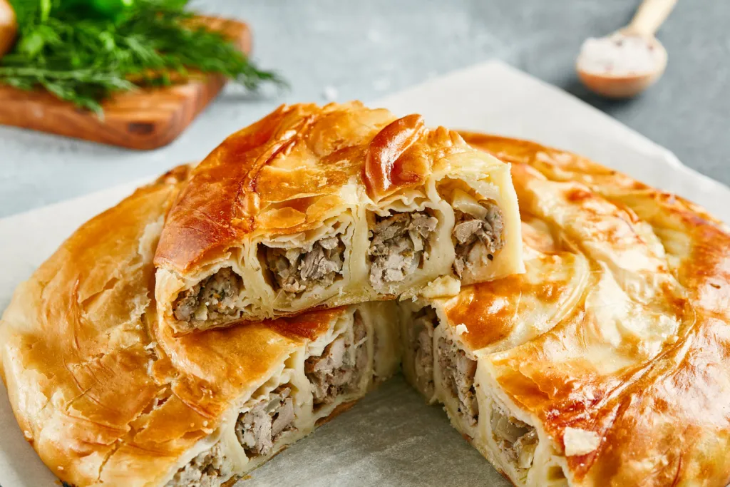 Classic pie with meat on wooden board. Composition with burek pie on concrete background with textile and spices. Balkan pie with minced meat in rustic style on gray table