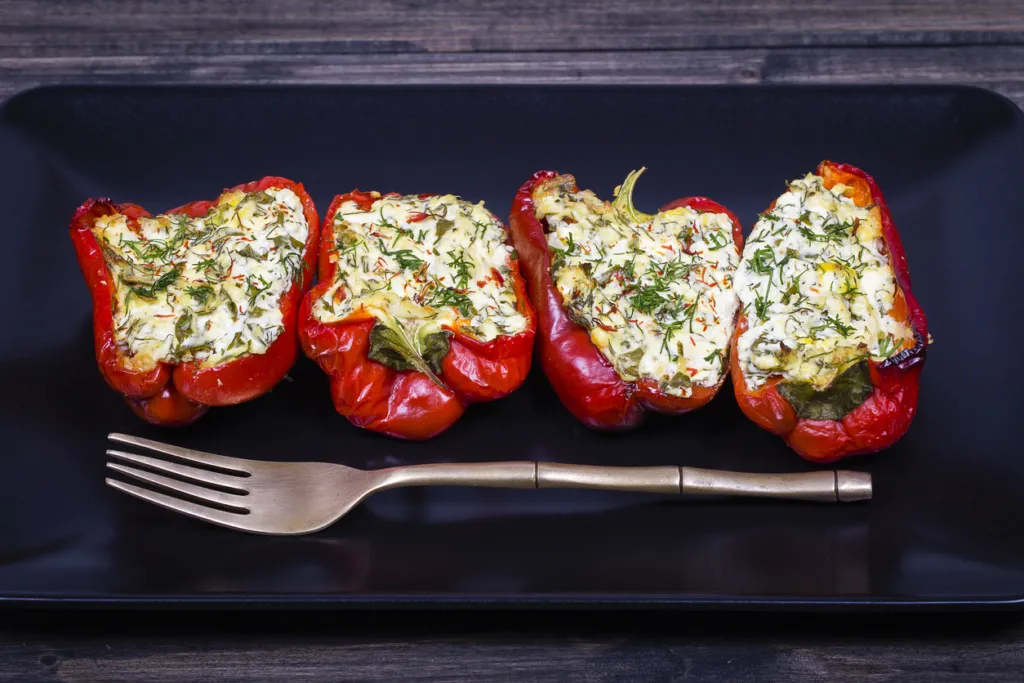 Red peppers stuffed with cream cheese with herbs and garlic, baked in grill in black plate, close up