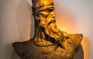 Texto antiguo: Busto de bronce de Skenderbeu, héroe nacional albanés, con armadura y casco tradicionales, expuesto en un museo de Albania.