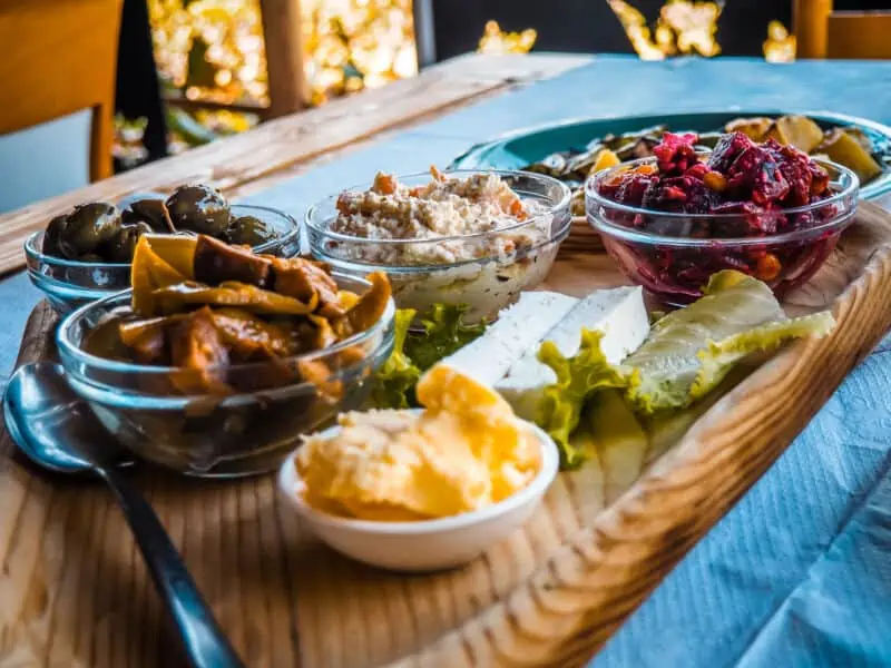 Frühstücksteller mit albanischen Spezialitäten, Oliven, Käse, Dipps, Salate und frisches Gemüse, auf Holzplatte, traditionell alpbanische Küche, Abenteuer Albanien.