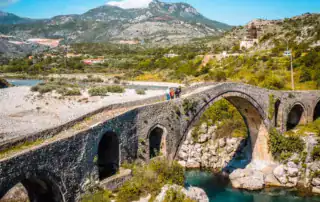 Paisaje alpino con puente de piedra en Albania, naturaleza verde, río y montañas, telón de fondo perfecto para la aventura Albania.