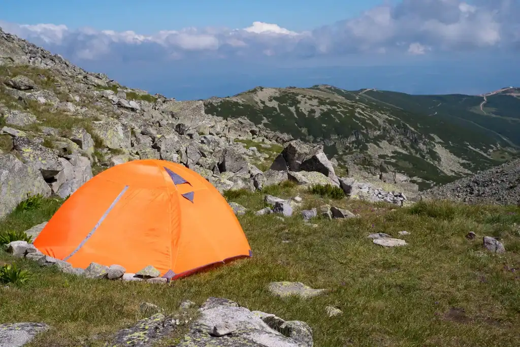 Camping in the mountains. Orange tent on the hill beneath the mountains.