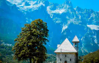 Majestuosas montañas albanesas con una iglesia tradicional en primer plano y un paisaje verde. Perfecto para aventuras en Albania y explorar la naturaleza.