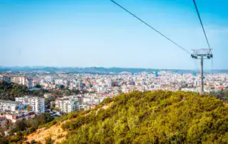 Teleférico en Tirana, Albania, sobre verdes colinas con vistas a la ciudad y al cielo azul, ideal para vivir aventuras y experiencias en la naturaleza en Albania.