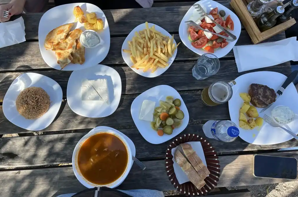 Albanian Food on table - foods are a bean soup, a spinach casserole, greek salad, goats cheese, fries, beef steak and bread