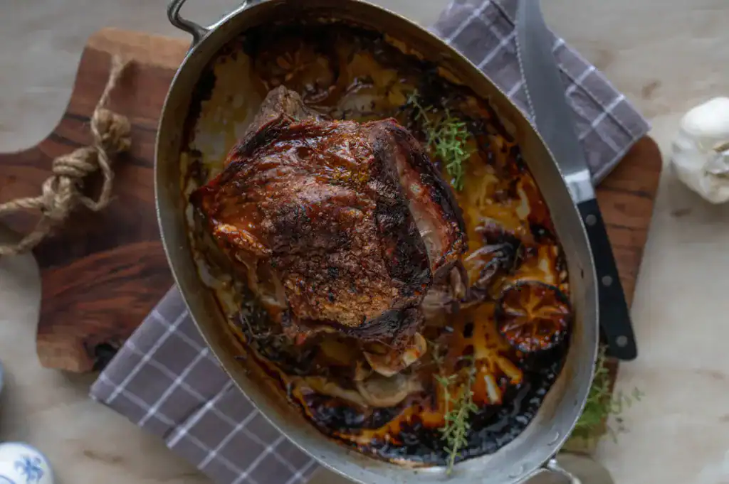Delicious homemade roasted turkey shank. Baked with lemon, thyme, garlic and served ready to eat in a rustic roasting pan on table background.