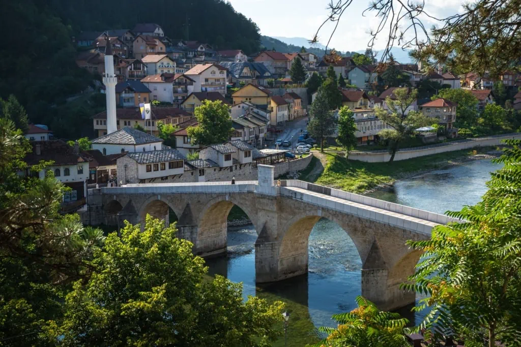 Historische brugpoort in een Albanese stad, omringd door traditionele huizen en groene bomen, met uitzicht op de rivier en de omringende heuvels - een typisch beeld van avontuur in Albanië.