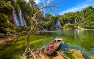Idílica cascada en Albania con barco en primer plano, naturaleza verde y aguas cristalinas, ideal para los amantes de la aventura y la naturaleza.