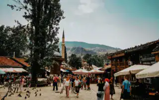Idílica plaza de mercado en Albania con arquitectura tradicional, gente, cafés y un panorama montañoso al fondo.