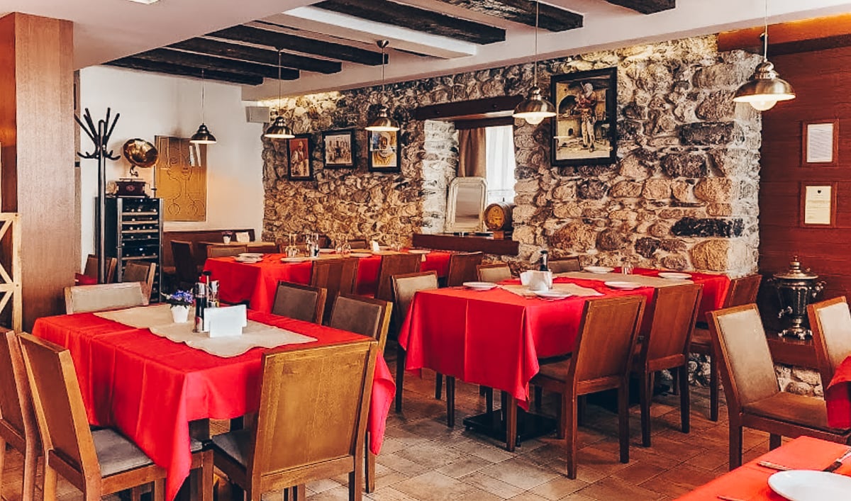 Rustykalna albańska restauracja z kamiennymi elementami, przytulną atmosferą, czerwonymi obrusami i drewnianymi meblami. Idealne miejsce, aby doświadczyć albańskiej kuchni i gościnności.