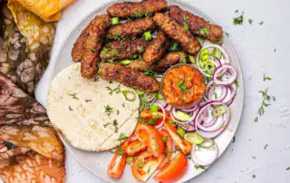 Crujientes chuletas de ternera albanesas con verduras frescas y salsa de tomate en un plato tradicional.