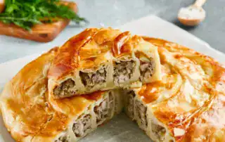 Grueso pastel de carne albanés con una crujiente cubierta de hojaldre, relleno de jugosa carne picada y cebolla, ideal para auténticas aventuras culinarias albanesas.