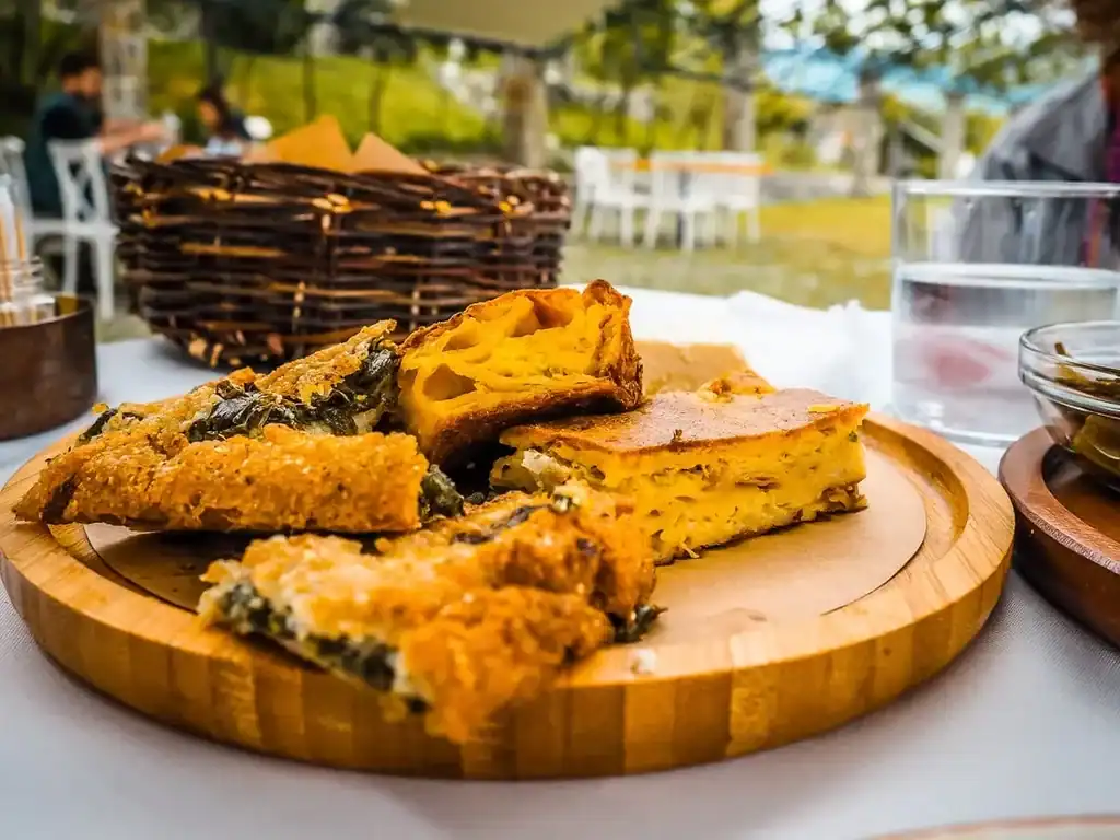 Knusprige albanische Spezialitäten und traditionelle Gerichte auf einem Holztablett, typische albanische Küche, Essen im Freien, Abenteuer Albanien, authentische lokale Küche, kulinarische Erlebnisreise.