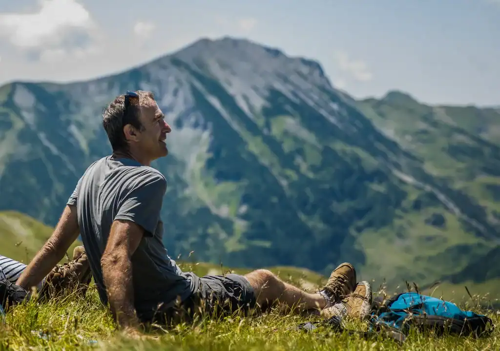 Oude man ontspant in de natuur op een bergweide met uitzicht op de indrukwekkende Albanese bergen, perfect voor avonturen in Albanië en het verkennen van de natuur.