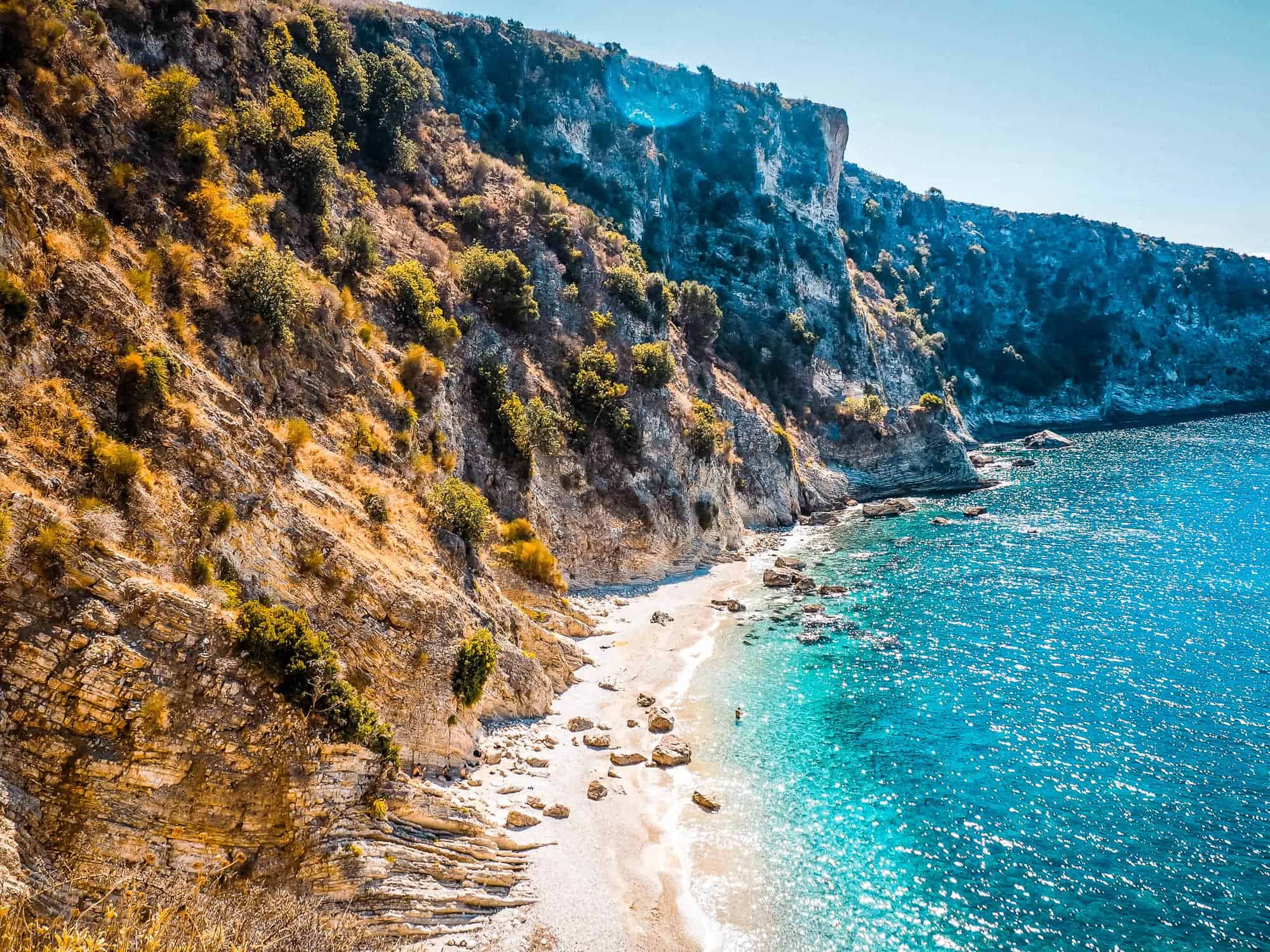 Bahía azul turquesa en la costa albanesa con escarpados acantilados, playas de arena clara y vegetación mediterránea, ideal para vivir experiencias de aventura y naturaleza en Albania.