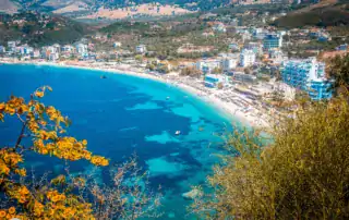 Pintoresca vista de las playas de Albania con aguas turquesas, rodeadas de modernos hoteles y montañas al fondo, ideal para viajeros de aventura y vacaciones.