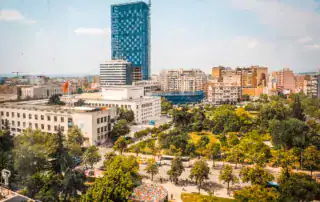 Paisaje urbano moderno en Tirana, Albania, con edificios altos, un parque urbano verde y lugares de interés cultural, ideal para los interesados en la naturaleza y la arquitectura.