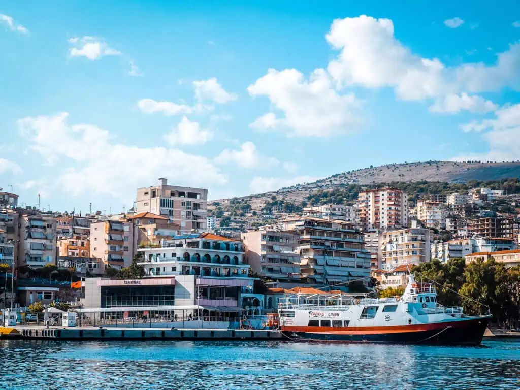 Bunte Hafenstadt in Albanien mit modernen Gebäuden, Yachthafen und Blick auf die Hügel im Hintergrund, geeignet für touristische Erkundungen und maritime Abenteuer.
