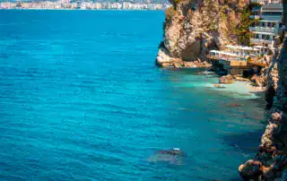 Bahías y acantilados de la costa albanesa con una vista del agua turquesa y la ciudad al fondo.
