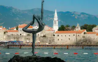 Elegante escultura de una bailarina frente al casco histórico de Budva, en Montenegro, con montañas al fondo: destino perfecto para los viajeros de aventura albaneses.