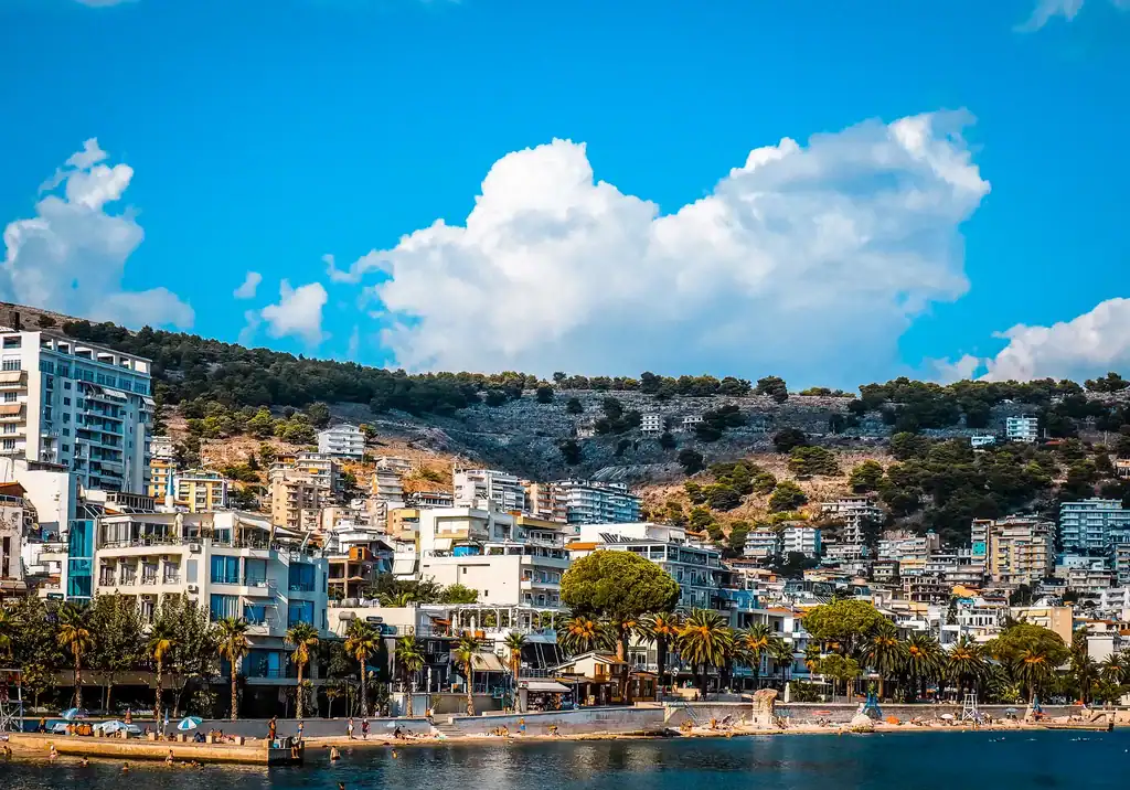Kleurrijke kuststad Saranda in Albanië met moderne gebouwen, palmbomen en bergen op de achtergrond, ideaal voor vakanties en reisavonturen.