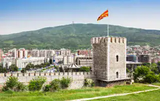 Historische stadsmuurtoren in Tetovo met Albanese vlag en uitzicht op de moderne stad op de achtergrond, omringd door groene bergen.