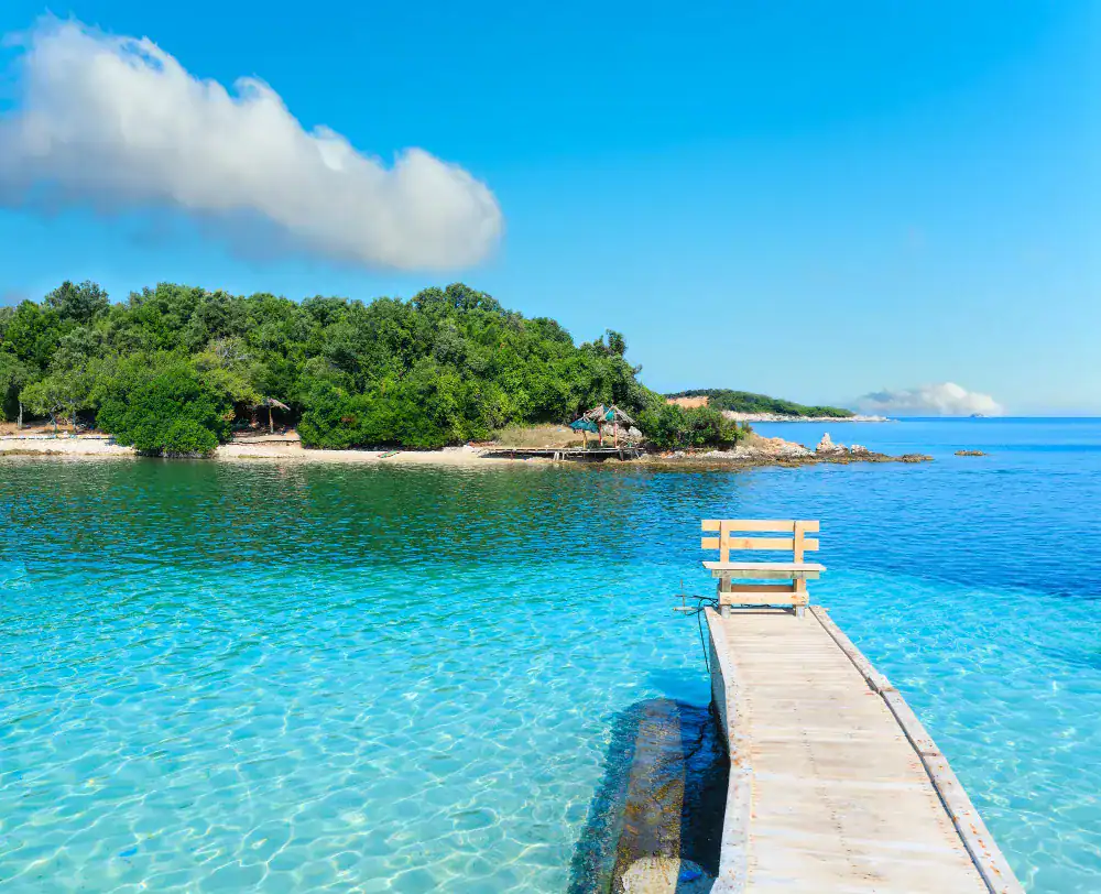 Beautiful Ionian Sea with clear turquoise water, wooden pier and morning summer coast view from beach (Ksamil, Albania)