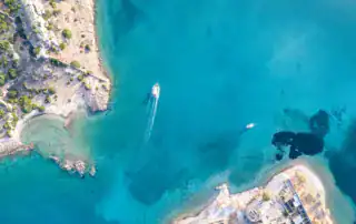 Lago de mar azul celeste en Albania con barcos y costa rocosa, destino ideal para la aventura y los deportes náuticos en la costa albanesa.