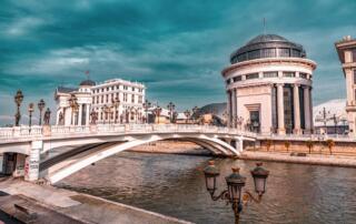 Fachada de edificio histórico con puente y río en Albania, cuna de las aventuras albanesas.