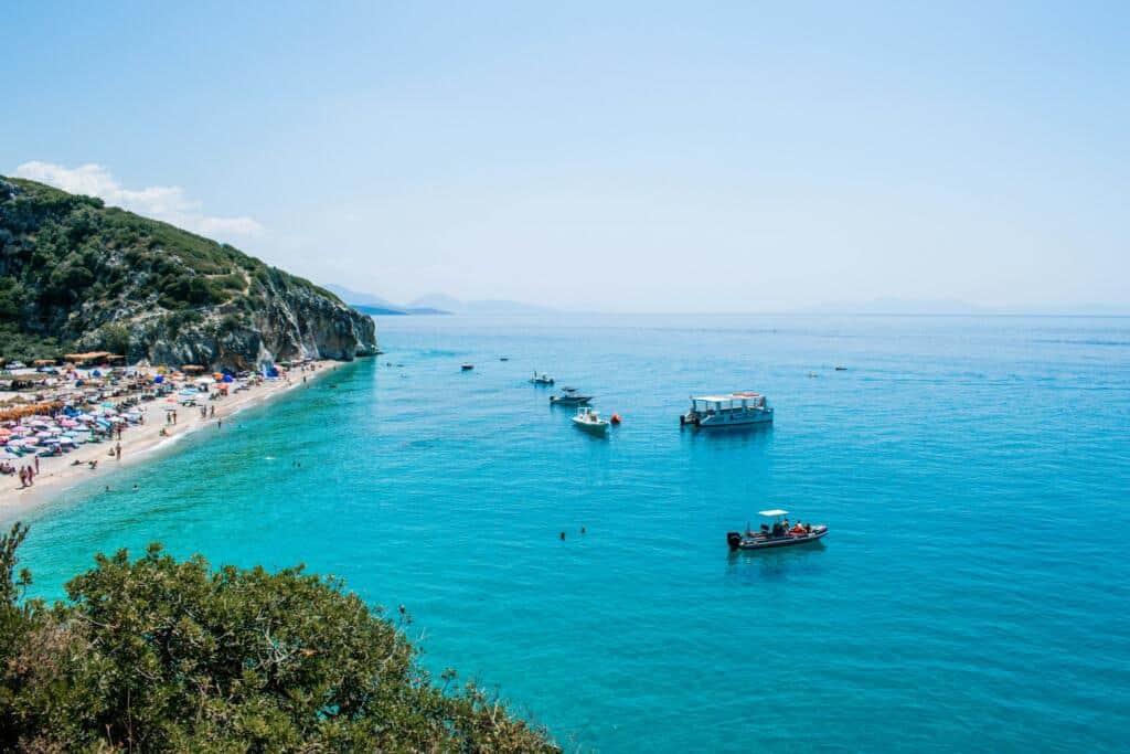 Pintoresca playa de la Riviera albanesa con aguas transparentes y coloridas tumbonas, región ideal para disfrutar del baño y la naturaleza en Albania.