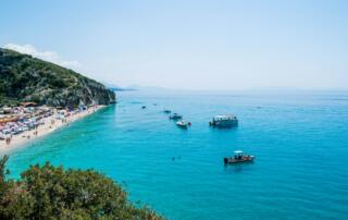 Pintoresca playa de la Riviera albanesa con aguas transparentes y coloridas tumbonas, región ideal para disfrutar del baño y la naturaleza en Albania.