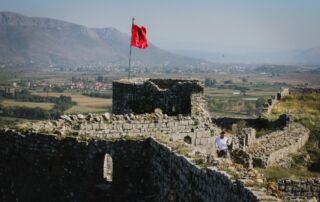 Ruinas del castillo en Albania con bandera albanesa, rodeado de un pintoresco paisaje de montañas y valles fértiles, ideal para la aventura Albania descubrir y senderismo.