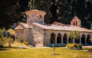 Altar de la iglesia en Albania, histórica iglesia bizantina con muros de piedra y tejado de tejas, rodeada de naturaleza y árboles, ideal para visitas religiosas y exploraciones culturales.