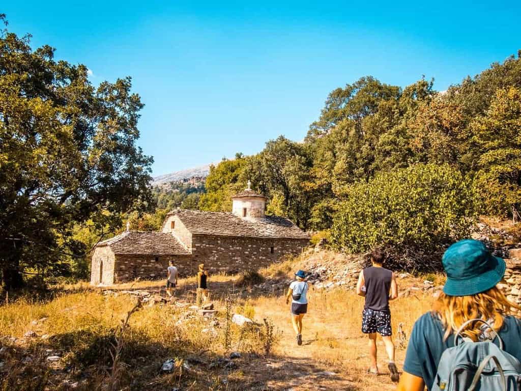 aventura albania paisaje con antiguos edificios de piedra y excursionistas caminando por un estrecho sendero a través de la naturaleza.