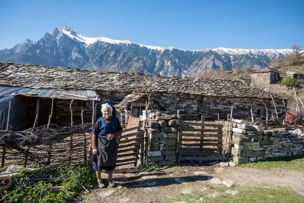 Antigua cabaña albanesa con montañas de fondo en los Alpes, arquitectura tradicional, escena rural, aventura Albania, naturaleza impresionante, auténtica vida de pueblo, montañas de fondo, patrimonio cultural, turismo Albania, paisaje virgen.