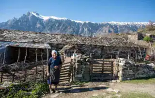 Cabaña albanesa con panorama de montaña, pueblo tradicional albanés, naturaleza alpina, modo de vida auténtico, aventura Albania.