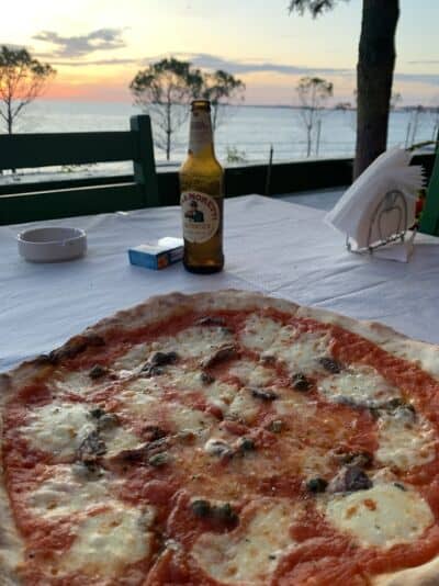 Pizza crujiente con tomate, queso y aceitunas en una mesa junto al mar al atardecer en Albania.