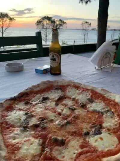 Knusprige Pizza mit Tomaten, Käse und Oliven auf einem Tisch am Meer bei Sonnenuntergang in Albanien.