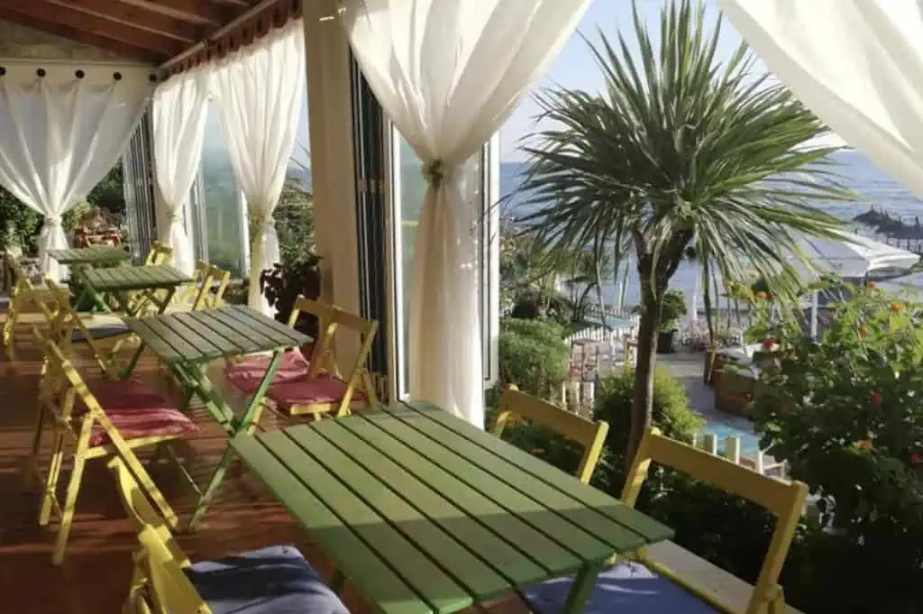 Strandpromenade in Albanien mit Blick auf das Meer, gemütlicher Außenbereich mit bunten Tischen und Palmen, ideal für eine Urlaubs- oder Erholungspause in der Natur.