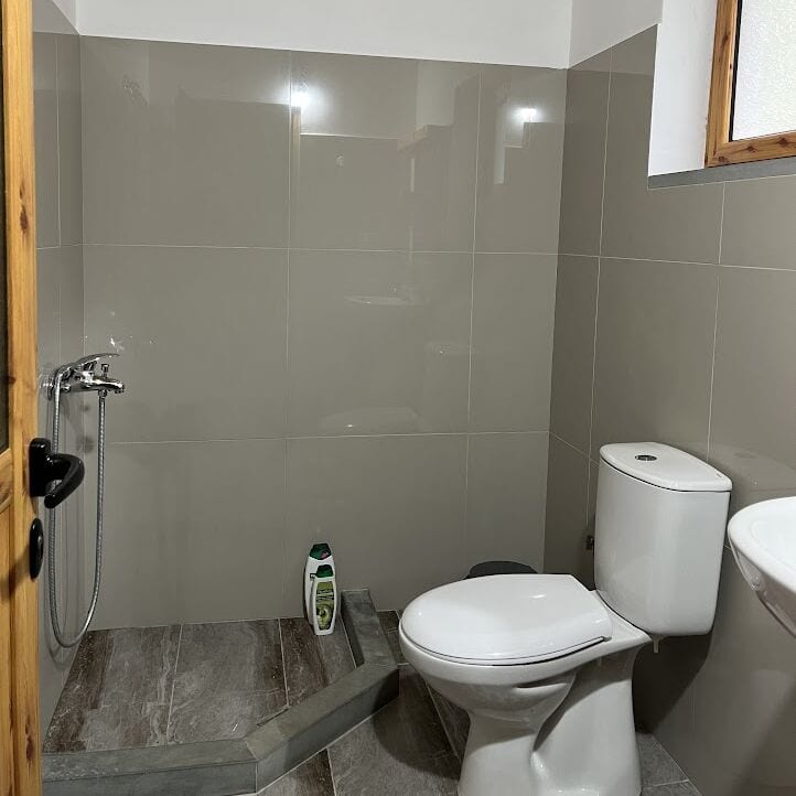 Baño alicatado en piedra natural con ducha, WC y pequeña ventana para ventilación natural, en el centro de Albania.