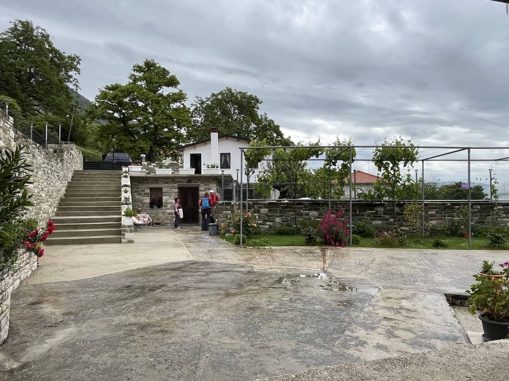 Bonito jardín albanés con plantas en flor, terraza de piedra y casa tradicional al fondo, perfecto para unas vacaciones de naturaleza y cultura en Albania.
