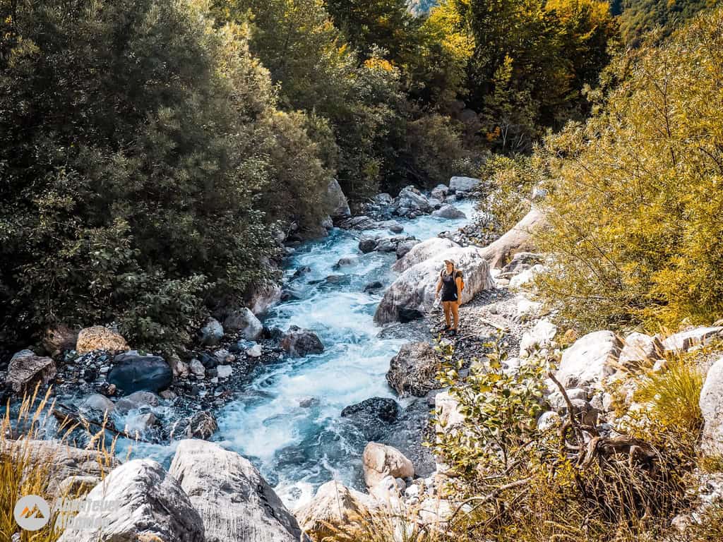 Adventure Albania: Wędrówka wzdłuż czystej górskiej rzeki w jesiennym lesie, w otoczeniu kolorowych liści, idealne tło dla miłośników przyrody i outdooru.