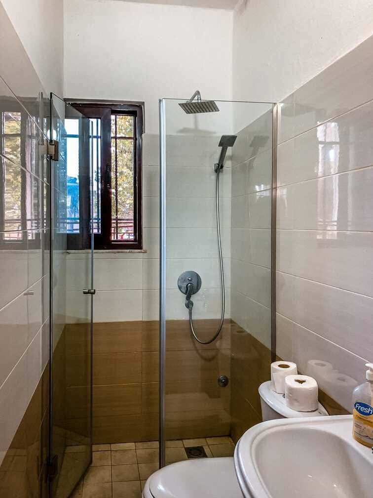 Cuarto de baño limpio con ducha a ras de suelo y accesorios modernos en un alojamiento con estilo en Albania. Perfecto para la comodidad y la relajación durante su viaje de aventura.